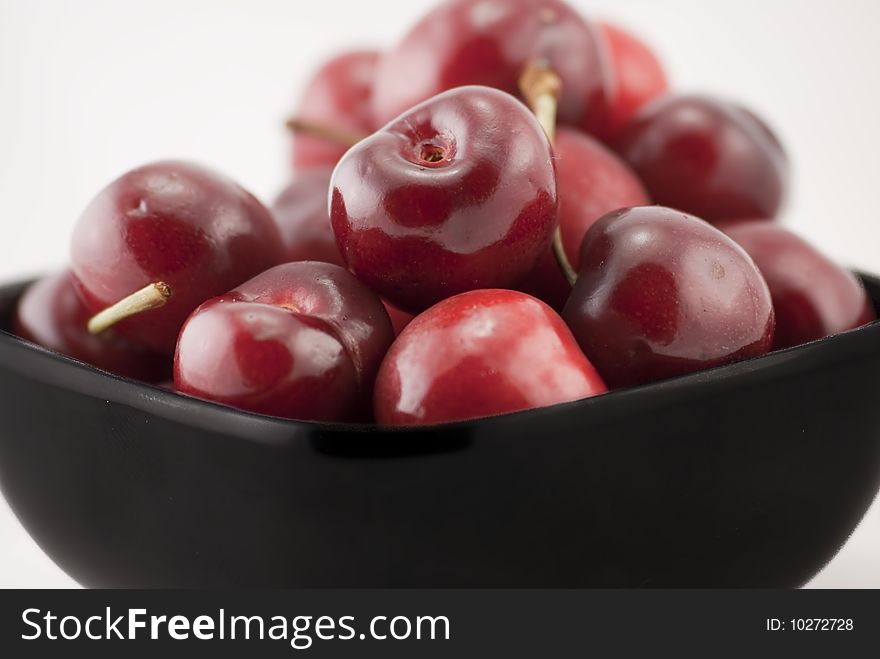 Black bowl of cherries isolated on white