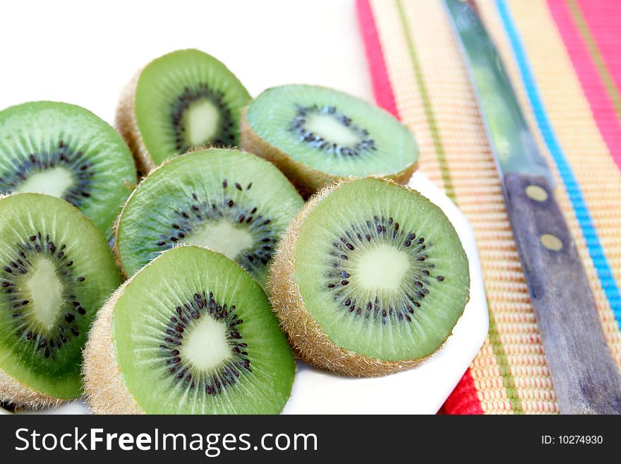 Slices of kiwi on a white plate with a colorful napkin to the side along with a knife. Slices of kiwi on a white plate with a colorful napkin to the side along with a knife.