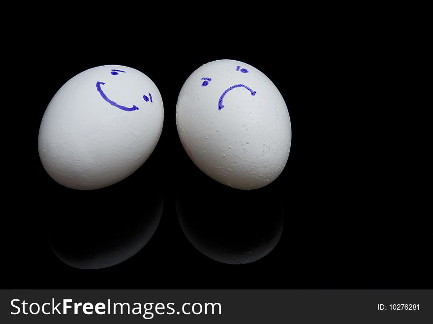 Composition of two white eggs with smiling and sad faces on black background. Composition of two white eggs with smiling and sad faces on black background