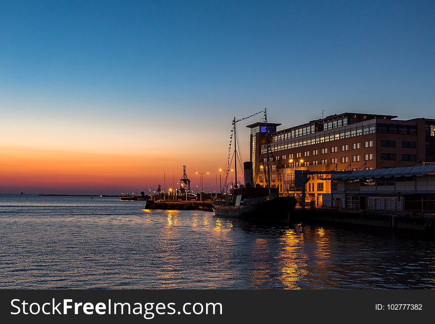 Boat And Dockside Buildings In Malmo Harbor At Sunset