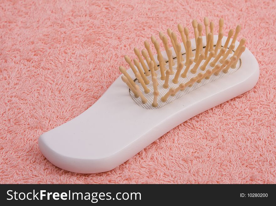 Wooden comb on peach-coloured bath towel. Hair comb close up.