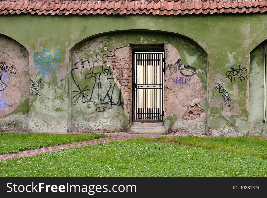 Metal openwork door in an ancient brick wall ornamented graffiti. Metal openwork door in an ancient brick wall ornamented graffiti