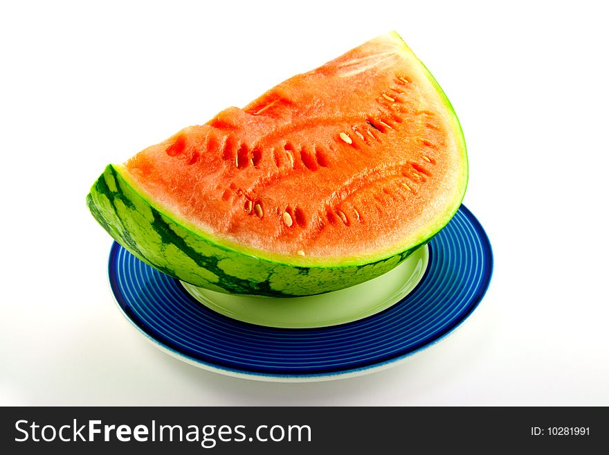 Slice of watermelon with green skin and red melon with seeds on a blue plate with a white background