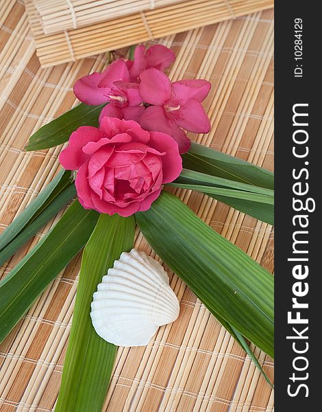 Decoration at the beautiful vacation: rose and oleander flowers set on a bamboo mat with a seashell and bamboo leaves