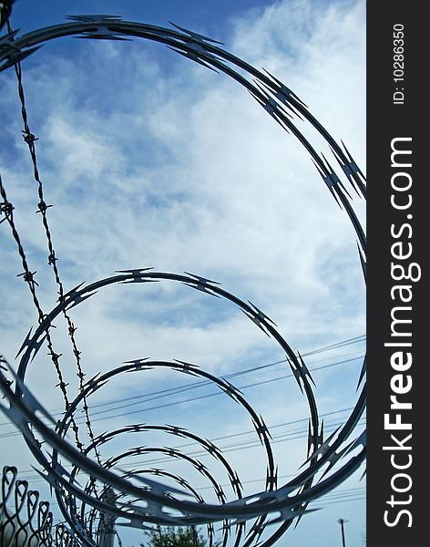 Loops of razor wire and barbed wire protective security fencing on top of a chainlink fence. Loops of razor wire and barbed wire protective security fencing on top of a chainlink fence