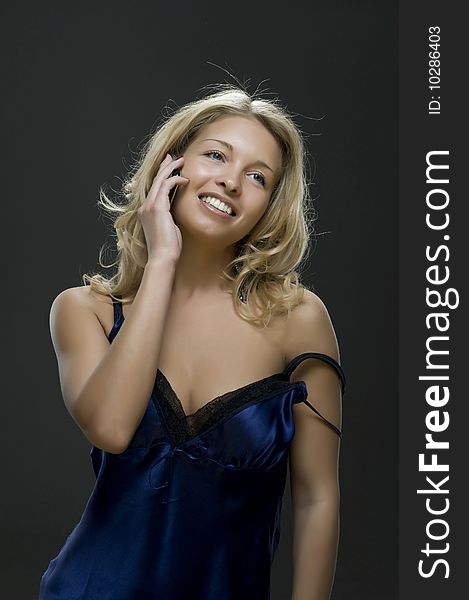 Young sexual girl blonde talks on a mobile telephone portrait in a studio on a dark background