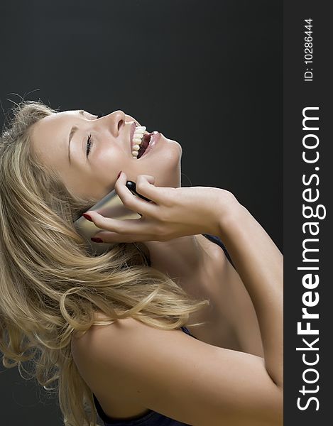 Young sexual girl blonde talks on a mobile telephone portrait in a studio on a dark background