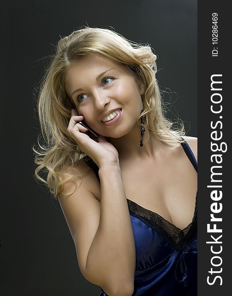 Young sexual girl blonde talks on a mobile telephone portrait in a studio on a dark background