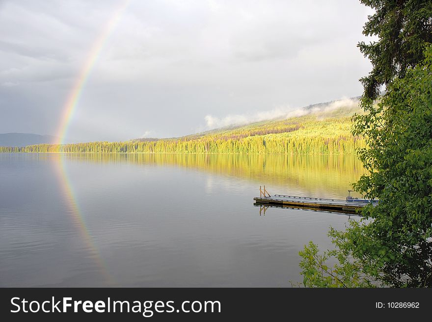 A rainbow forms over a calm forested lake. A rainbow forms over a calm forested lake