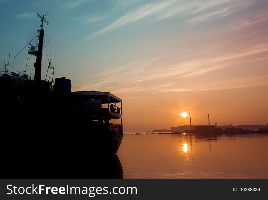 A sillhoutte of cargo ship docking at port, taken early in morning, when red and golden sunrise blending into the blue morning sky. A sillhoutte of cargo ship docking at port, taken early in morning, when red and golden sunrise blending into the blue morning sky