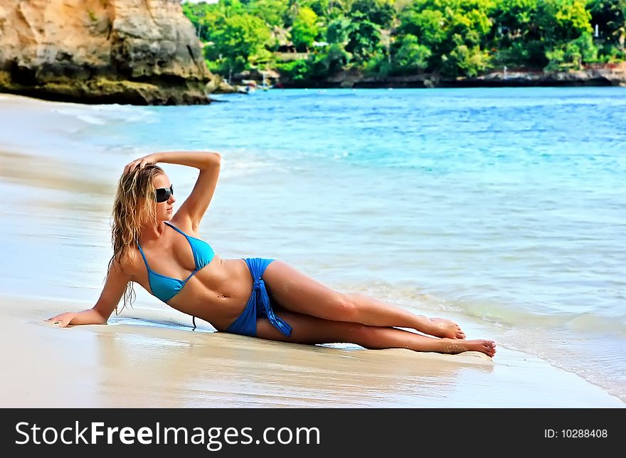 Blond girl in sunglasses lying on the beach with reflection in water. Blond girl in sunglasses lying on the beach with reflection in water