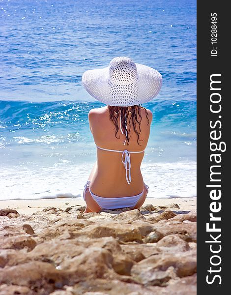 Beautiful brunette with long hair in white hat and swimsuit sits on the sand ocean beach on Bali in Indonesia. Beautiful brunette with long hair in white hat and swimsuit sits on the sand ocean beach on Bali in Indonesia