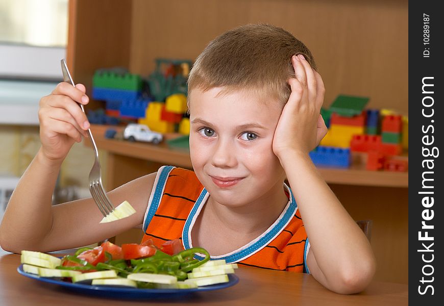 The little boy eats fresh salad on the table. The little boy eats fresh salad on the table