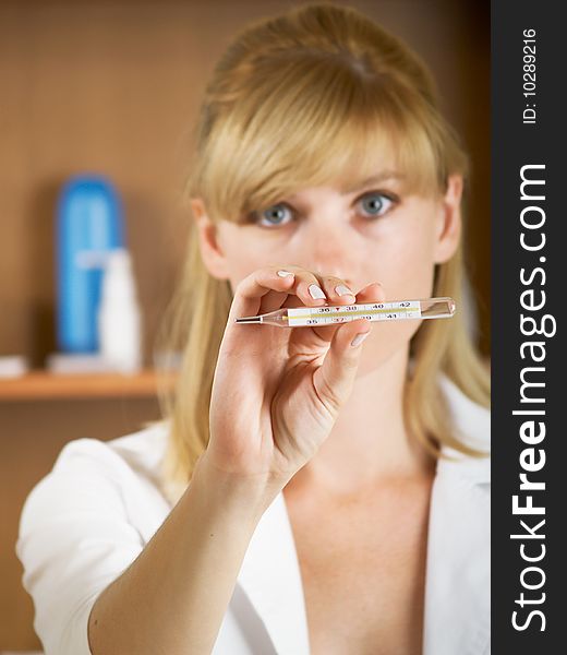 Closeup portrait of beautiful young female doctor looks at a thermometer. Closeup portrait of beautiful young female doctor looks at a thermometer