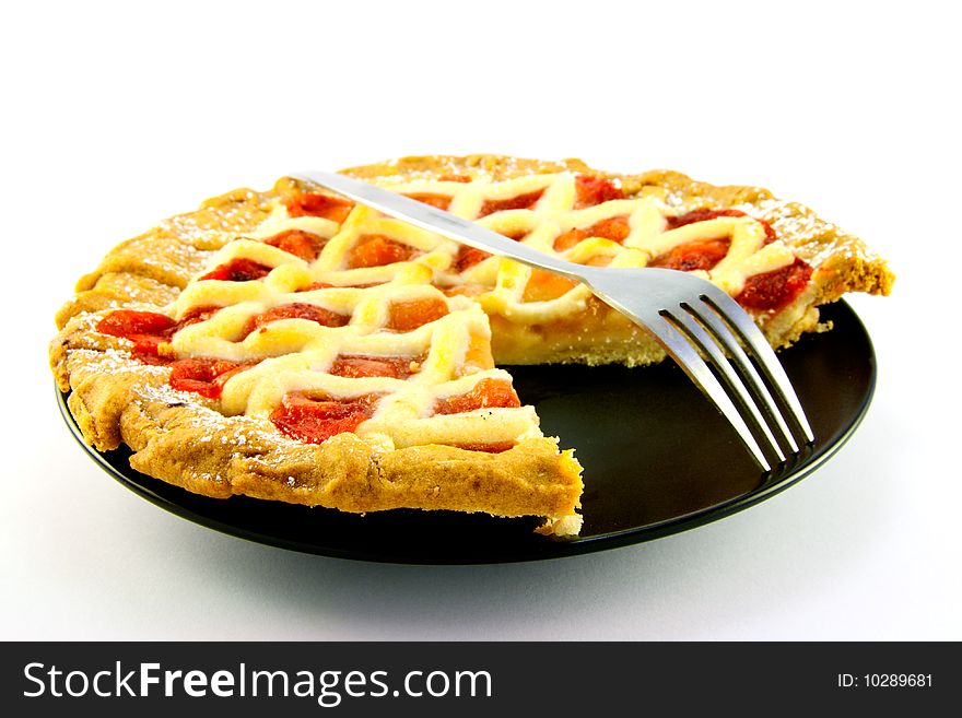 Whole apple and strawberry pie with a small fork on a black plate with a slice missing on a white background. Whole apple and strawberry pie with a small fork on a black plate with a slice missing on a white background