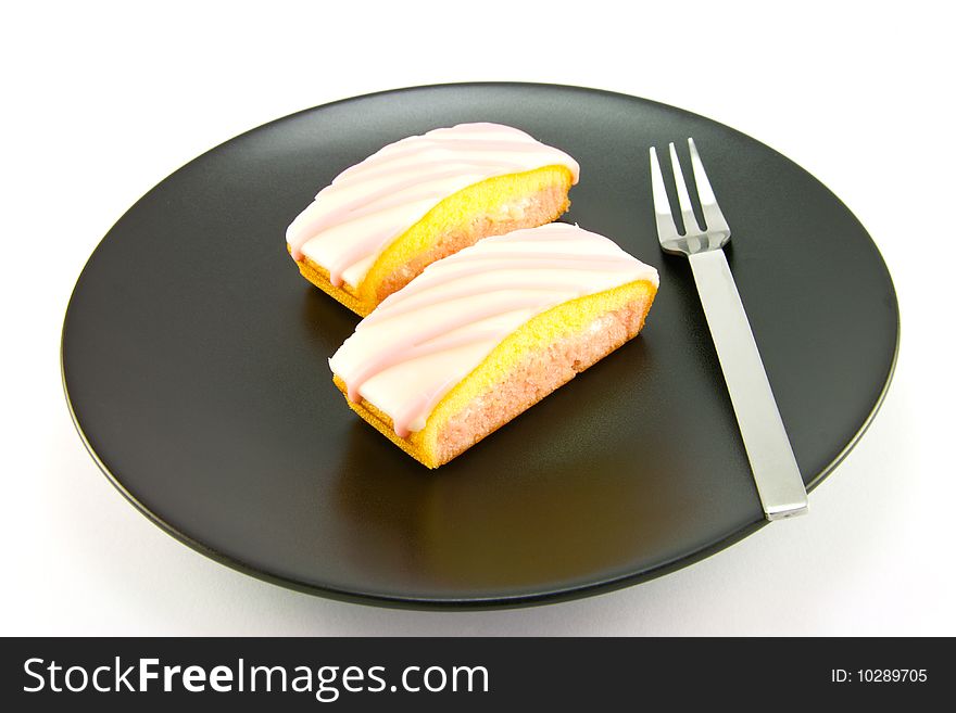 Two pink strawberry sliced cakes with icing on the top with a small fork on a black plate with a white background. Two pink strawberry sliced cakes with icing on the top with a small fork on a black plate with a white background