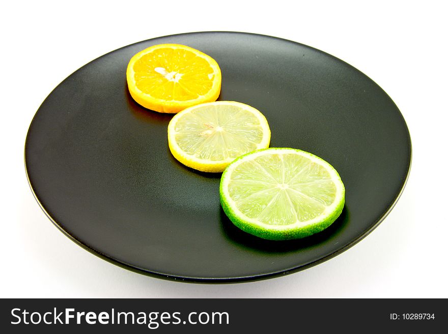 Lemon, lime and orange slices in a line on a black plate on a white background. Lemon, lime and orange slices in a line on a black plate on a white background