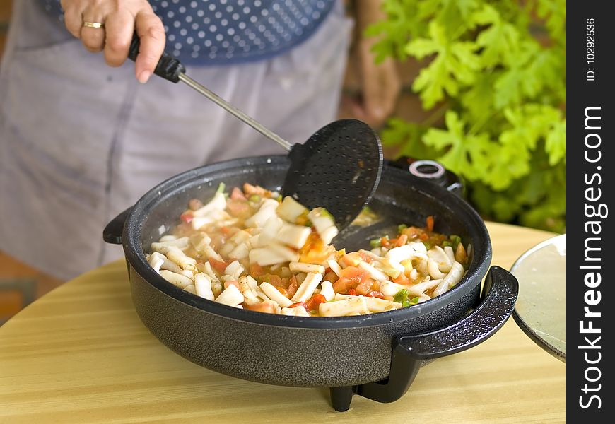 Woman cooking paella. This is the first step: Saute the squids with the vegetables.