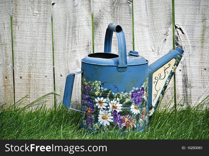 Decorative watering can by an old fence. Decorative watering can by an old fence.