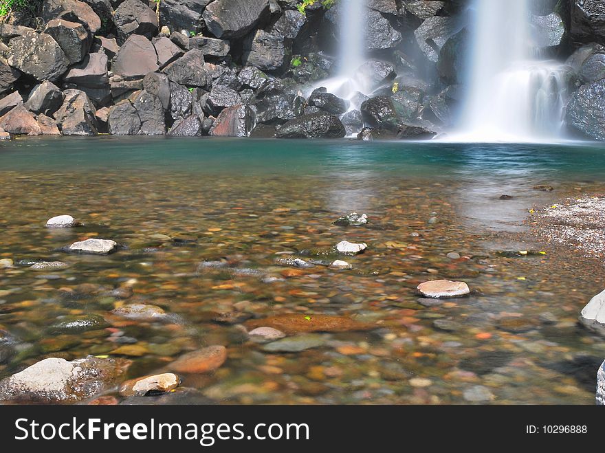 Low shot of majestic waterfall into pool of pebbles