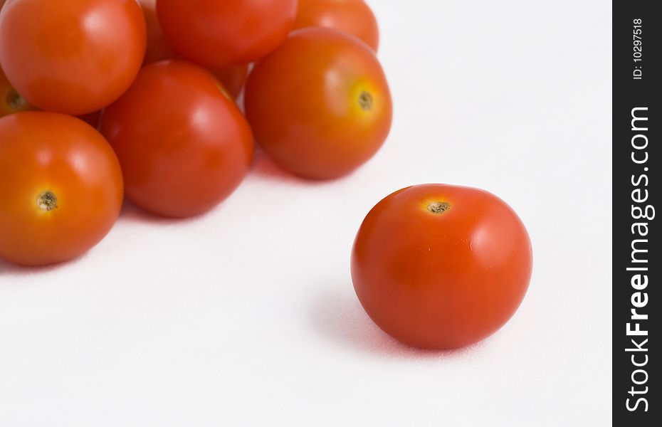 A single cherry tomato in front of a pile of other cherry tomatoes on a white background