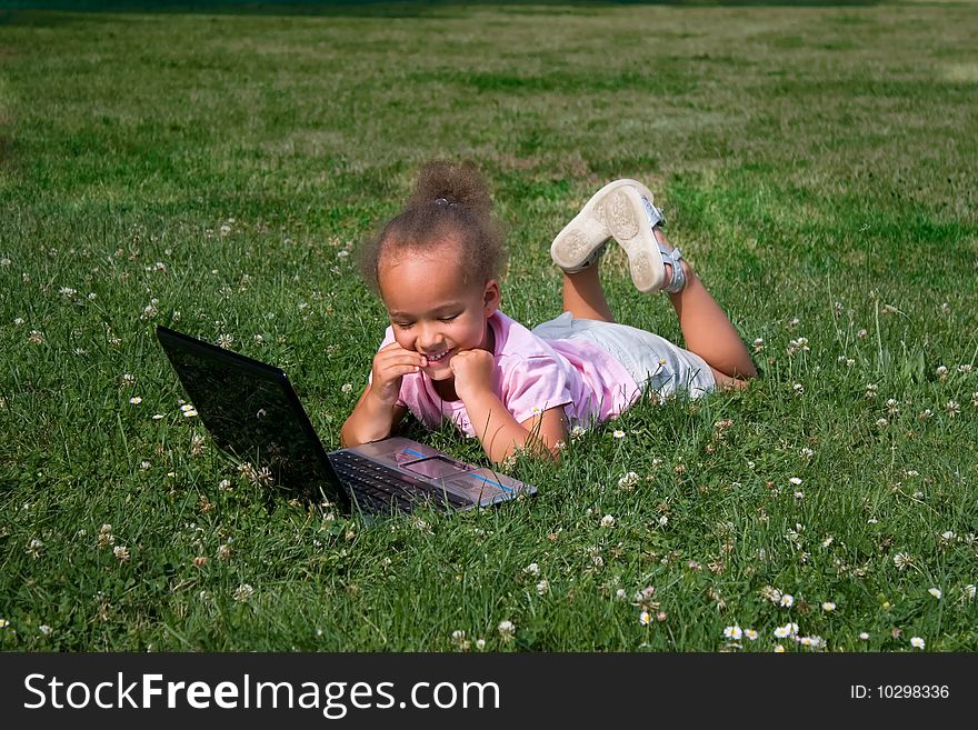 A young ethnic girl plays with the wireless laptop computer while lying in the green grass. A young ethnic girl plays with the wireless laptop computer while lying in the green grass.