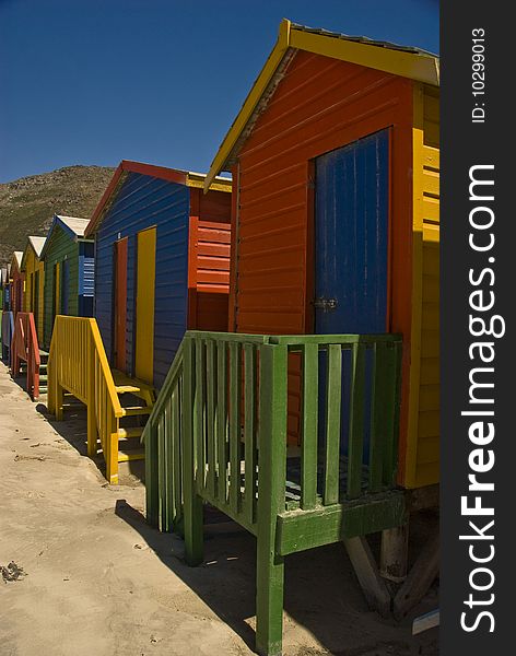 Brightly colored beach huts  standing in a long line on a beach. Brightly colored beach huts  standing in a long line on a beach