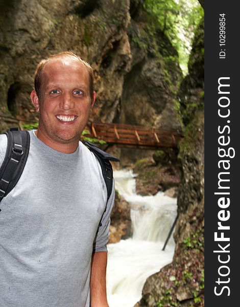 Young man is hiking on a trail in the mountains. A big waterfall in the background - focus on the young man. Young man is hiking on a trail in the mountains. A big waterfall in the background - focus on the young man.