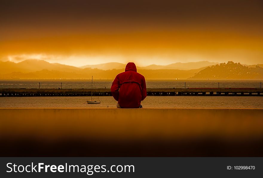 Person Wearing Red Hoodie Sitting In Front of Body of Water