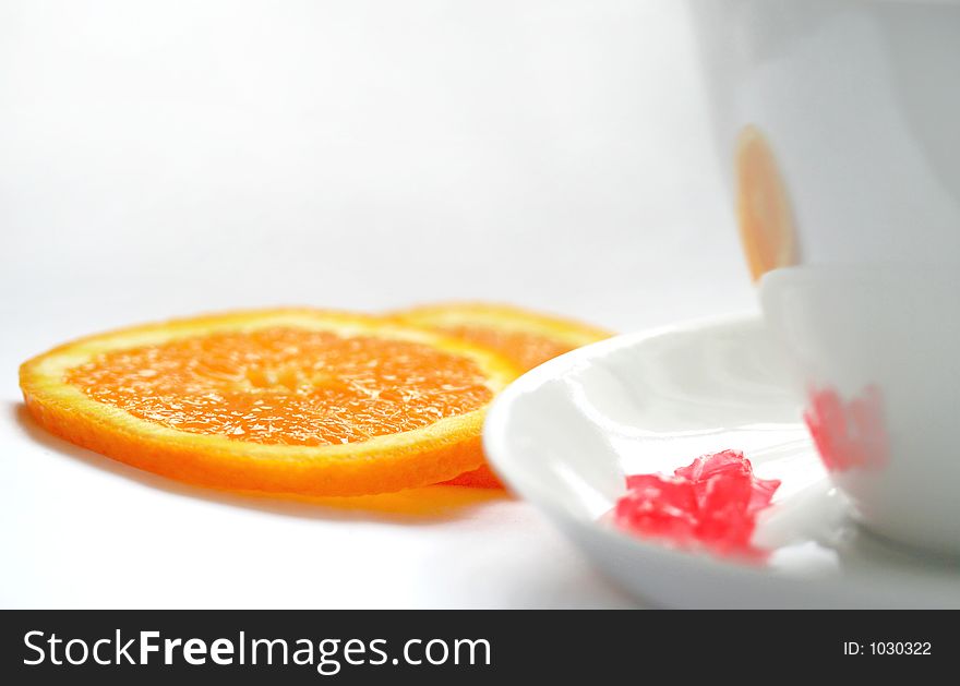 White cup on a white background. An orange. Red sweets /candies/