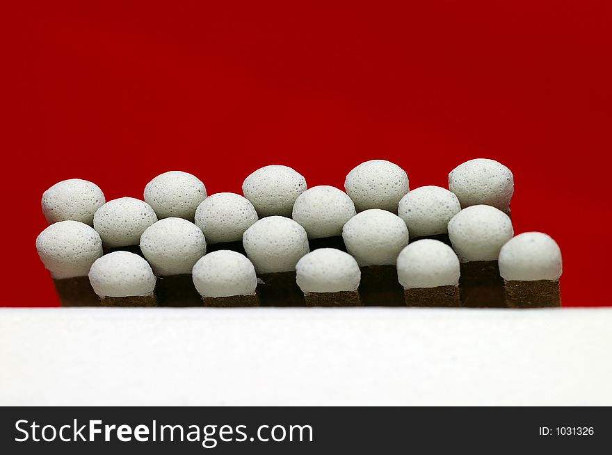 Closeup of White Tipped paper match heads against a bright red background