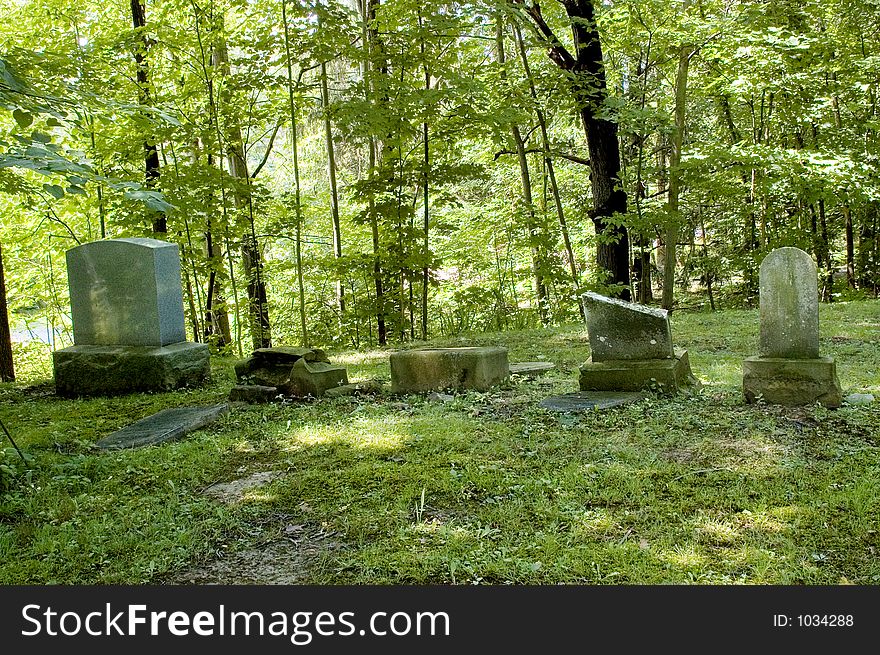 A row of early grave markers in a country cemetery.  Stones are very old, broken and weathered. Contrasted by the new headstone at the far left of the image. A row of early grave markers in a country cemetery.  Stones are very old, broken and weathered. Contrasted by the new headstone at the far left of the image