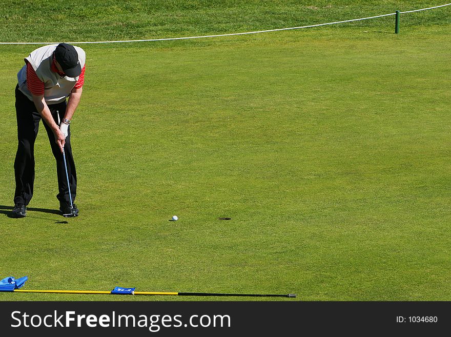 Golfer putting the ball into the hole in a tournament, ball heading towards hole. Golfer putting the ball into the hole in a tournament, ball heading towards hole