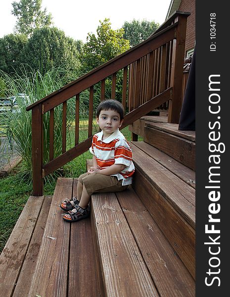 Toddler boy sitting on deck steps.