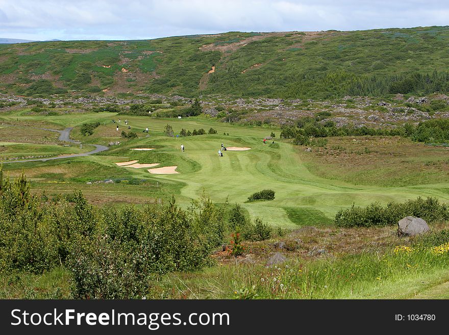 A green golfcourse on a overcast day, people on the greens playing golf. A green golfcourse on a overcast day, people on the greens playing golf