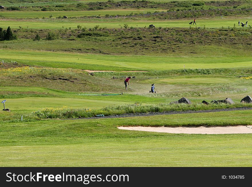 A green golfcourse on a overcast day, people on the greens playing golf