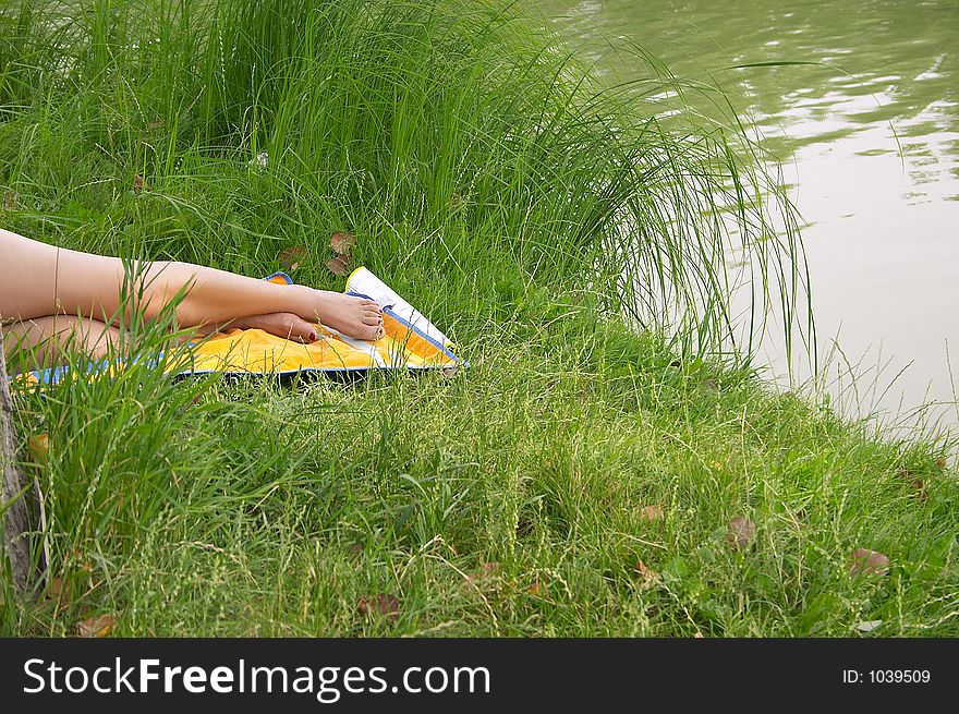 Legs of a tanning girl laying in the grass on the bank of a lake