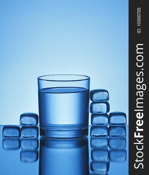 Glass of water and ice cubes on blue background