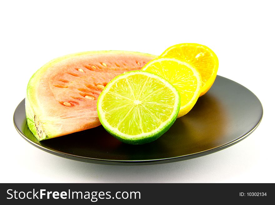 Slice of red juicy watermelon with a slice of lemon, lime and orange on a black plate with a white background. Slice of red juicy watermelon with a slice of lemon, lime and orange on a black plate with a white background