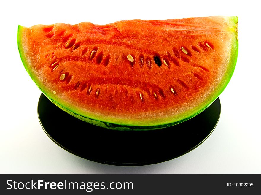 Slice of watermelon with green skin and red melon with seeds on a black plate with a white background. Slice of watermelon with green skin and red melon with seeds on a black plate with a white background