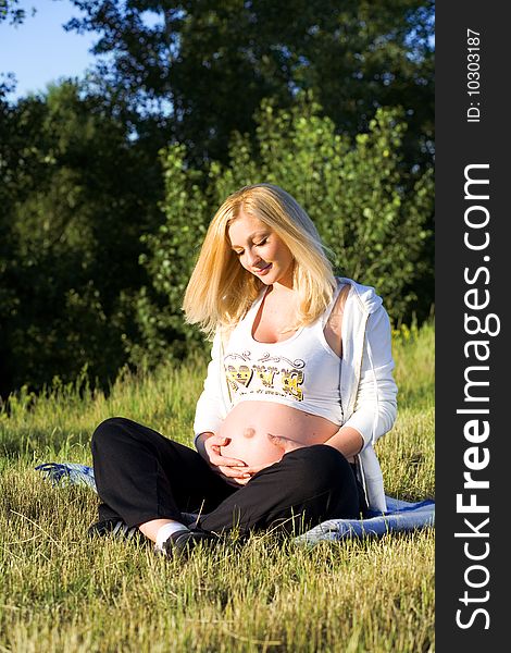 Beautiful pregnant woman sitting on the grass and looking on belly