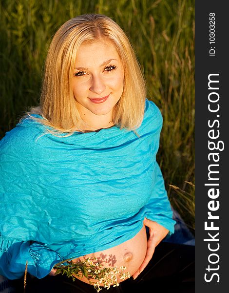 Beautiful pregnant lady sitting on the grass with flowers in the hand