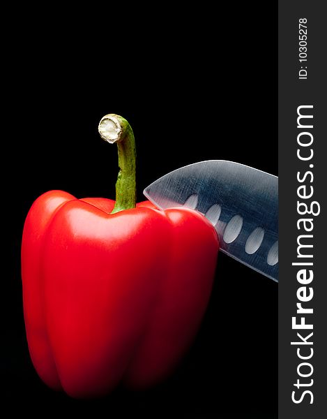 A red pepper being sliced on a dark background