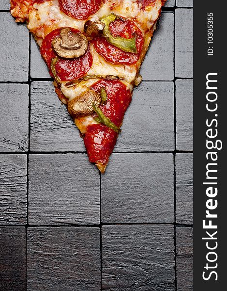 A slice of pizza on a black wooden background