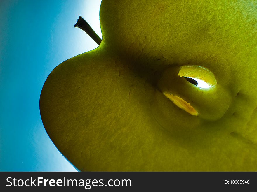 Slice of green apple is backlighted and on blue background. Slice of green apple is backlighted and on blue background