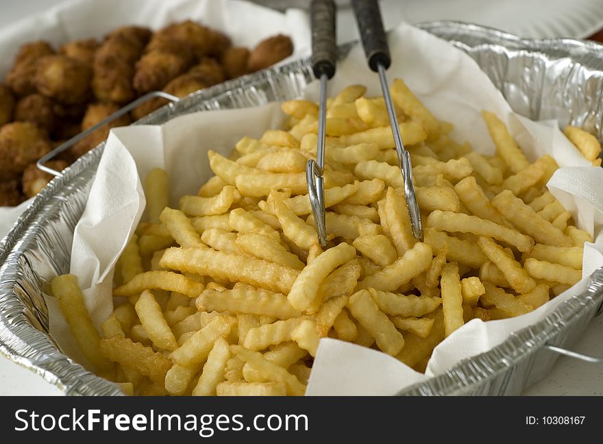 A large pan of deep fried golden brown french fries ready for serving, horizontal with shallow depth of field