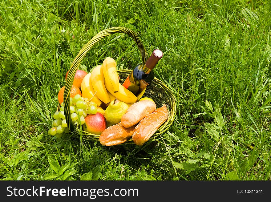 Baking a fruit basket and a bottle of wine on the green grass. Baking a fruit basket and a bottle of wine on the green grass