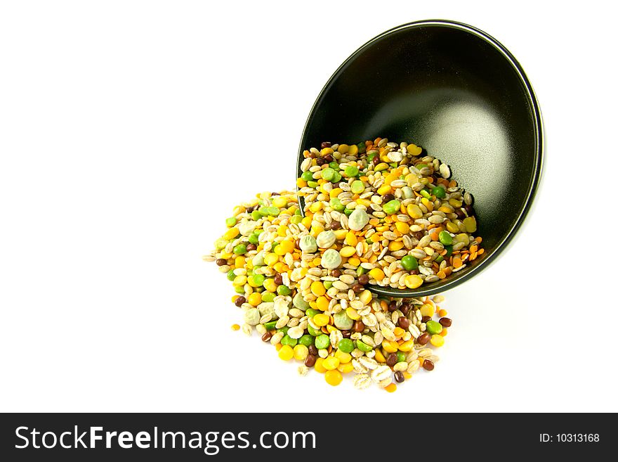 Assorted soup pulses spilling from a round black bowl on a white background. Assorted soup pulses spilling from a round black bowl on a white background