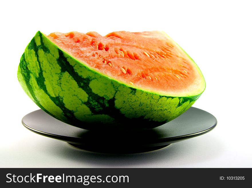 Slice of watermelon with green skin and red melon with seeds on a black plate with a white background. Slice of watermelon with green skin and red melon with seeds on a black plate with a white background