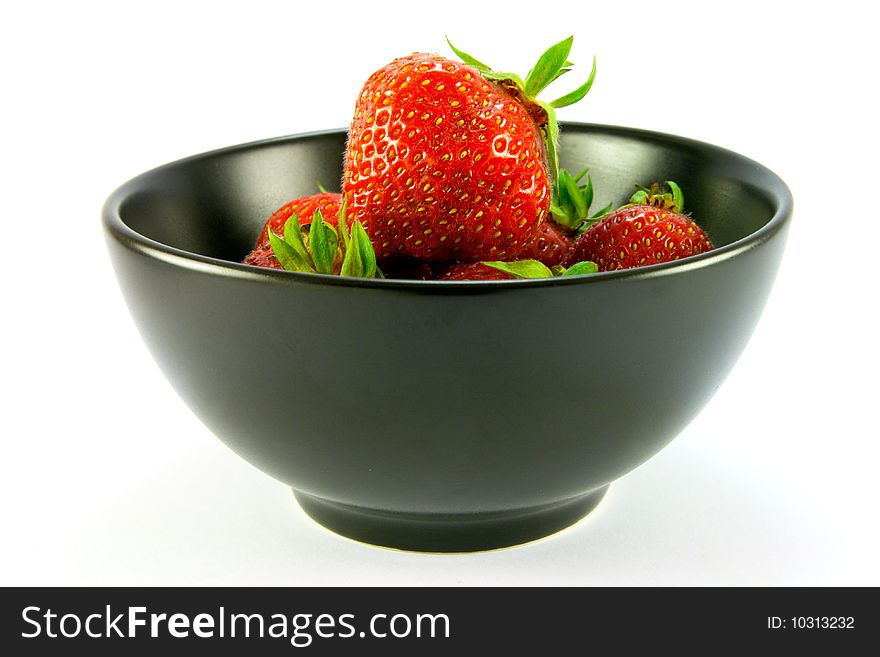 Whole red ripe strawberries in a black bowl on a white background